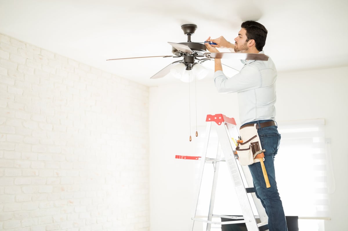 Technician on a ladder completing ceiling fan installation
