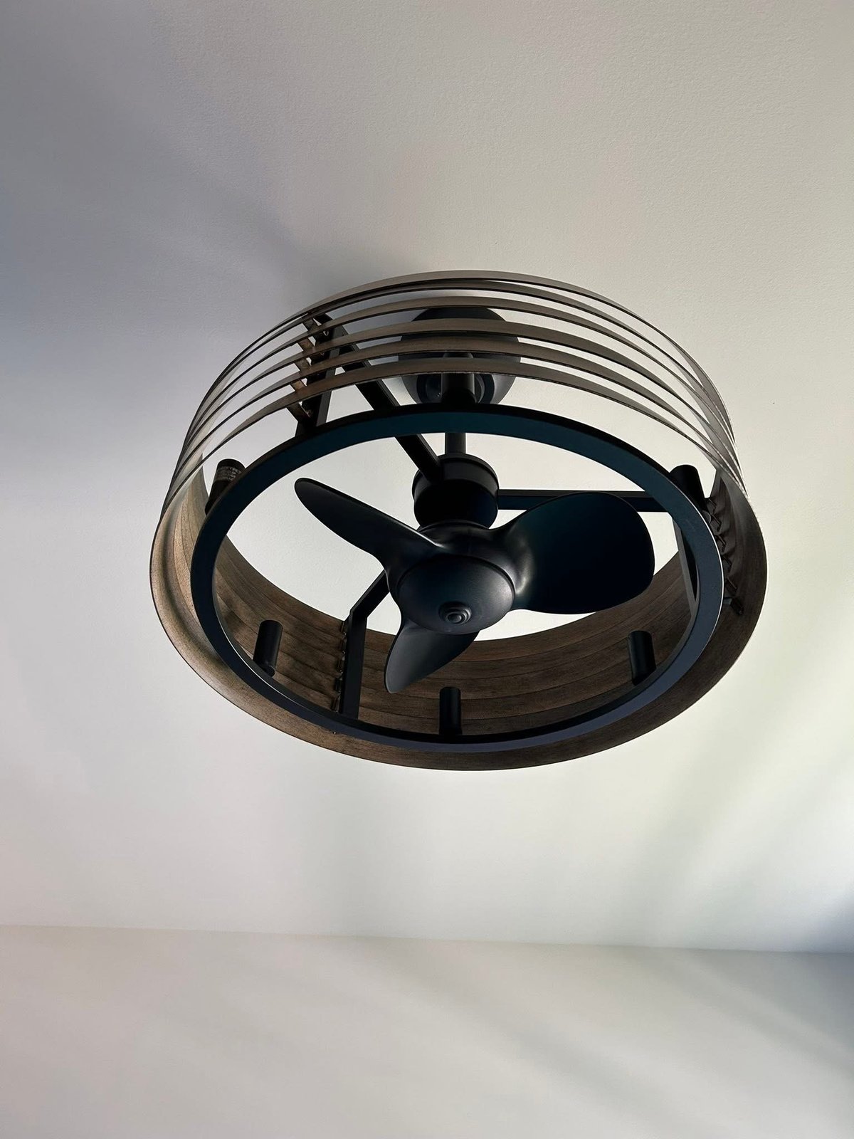 Modern ceiling fan with black metal cage design and three-blade fan mounted on white ceiling