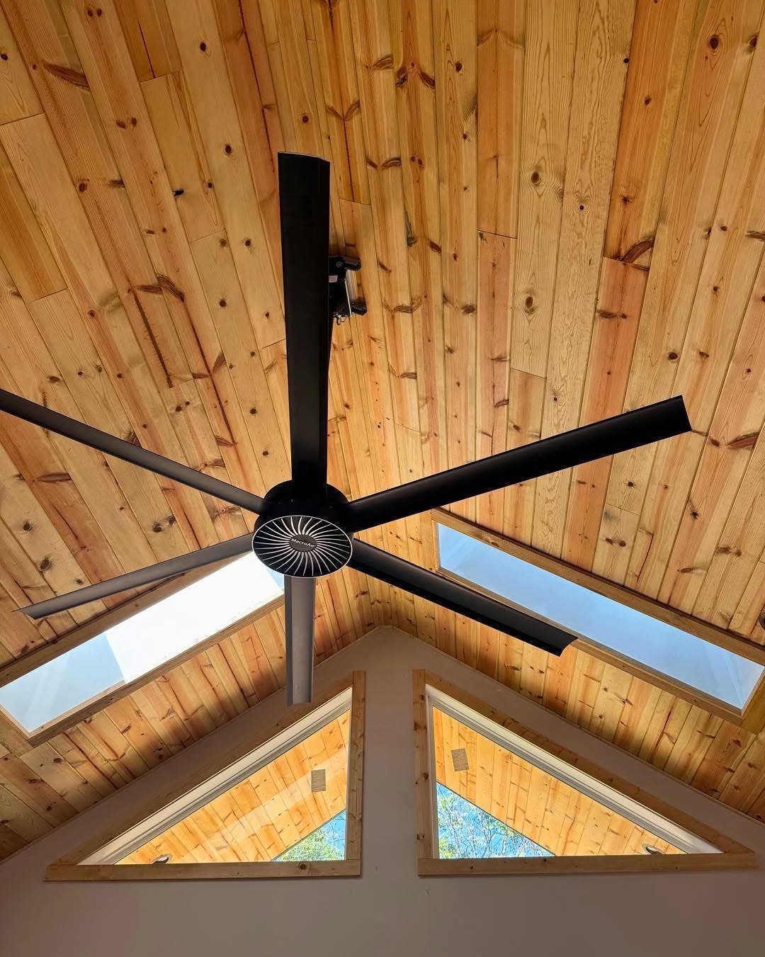 Black ceiling fan mounted on a wooden cathedral ceiling with triangular skylights