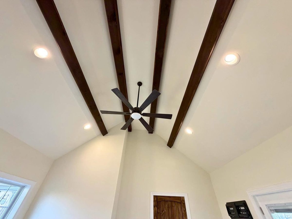 Vaulted ceiling with dark wooden beams, recessed lights, and a modern ceiling fan in the center