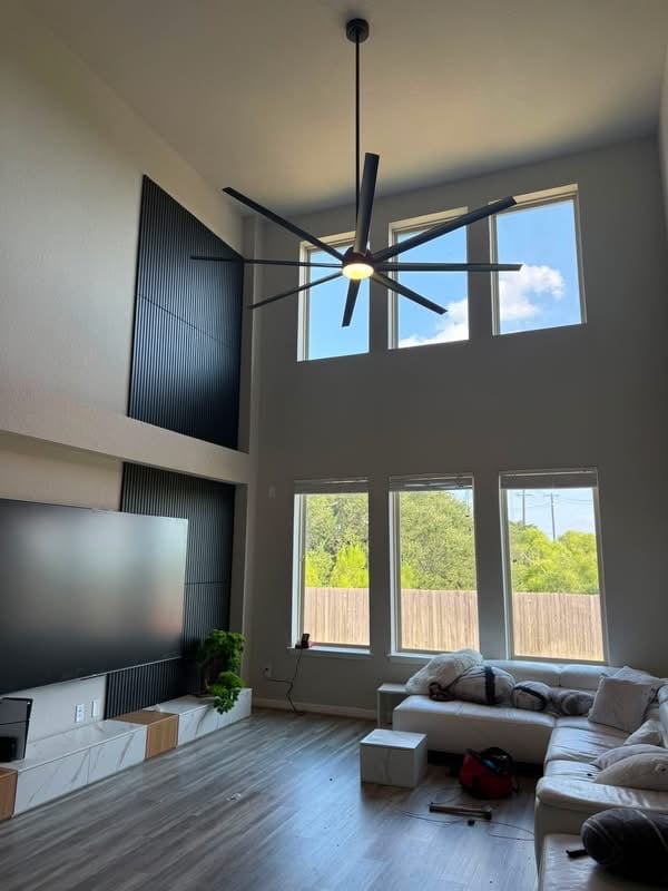 Modern living room with a high ceiling, large windows, TV stand, large black ceiling fan, and sectional sofa overlooking an outdoor deck